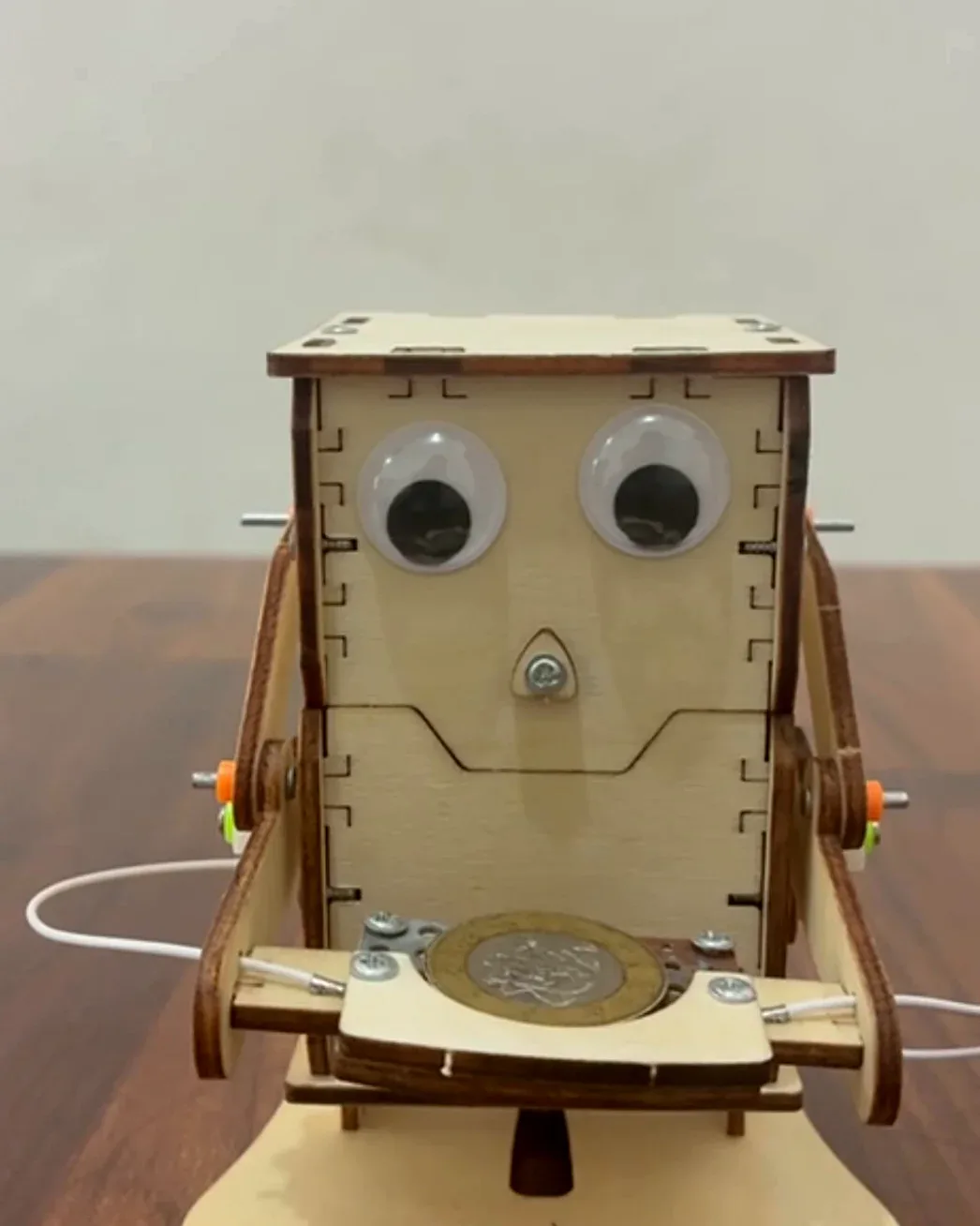A small wooden robot with googly eyes and a coin slot