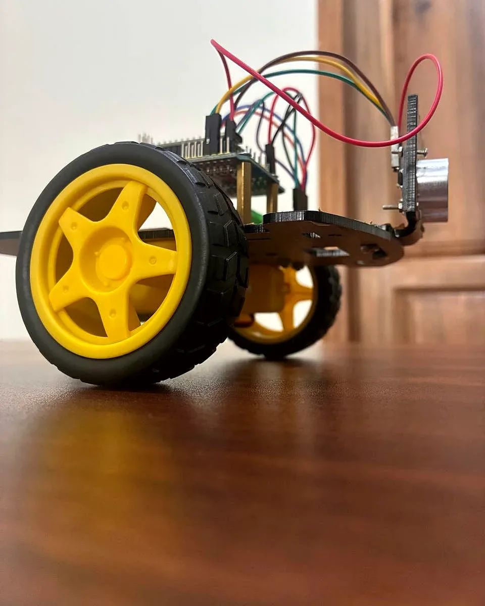 A robot car with a large yellow wheel on a wooden table